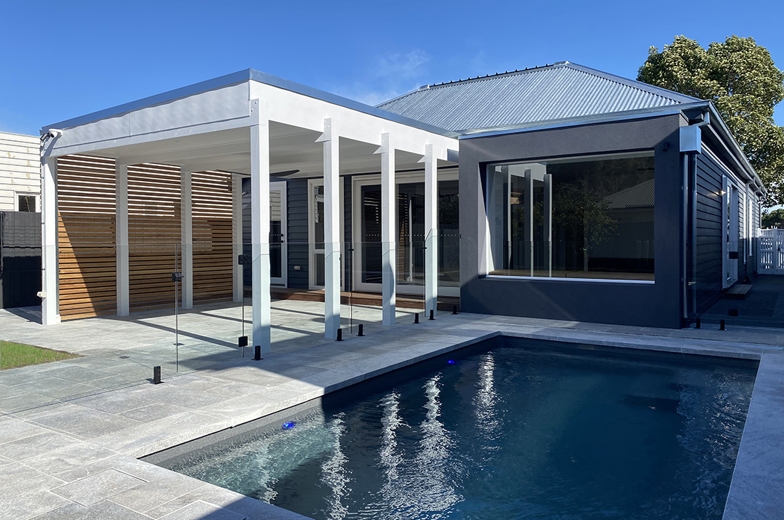 Modern extension to the rear of a traditional heritage home by local Williamstown architect Dig Design featuring a large window seat overlooking a swimming pool surrounded with bluestone paving. A roofed white pergola covering an outdoor entertainment area is next to the pool.