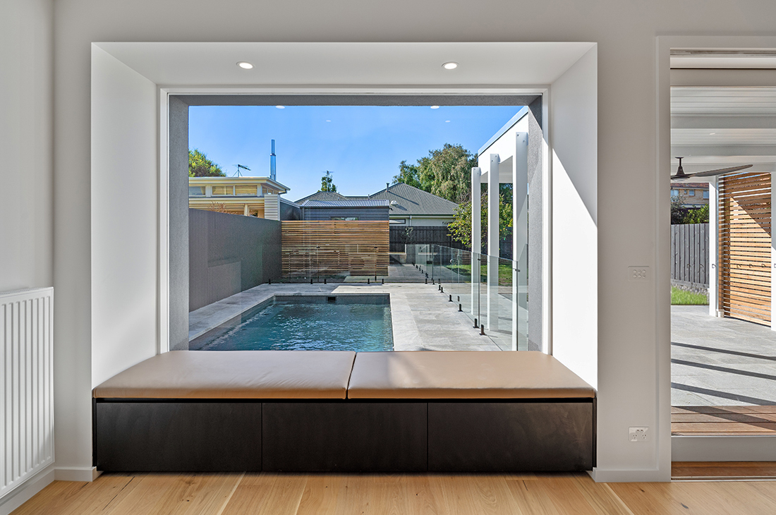 A large modern window seat looks out from the living room onto the swimming pool. Lots of natural light fills the space and it looks like a comfy place to curl up on the tan leather upholstery with a good book.