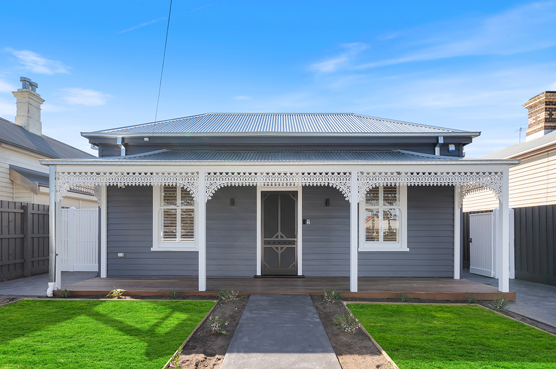 Modern extension to the rear of a traditional heritage home by local Williamstown architect Dig Design. An exposed aggregate concrete path leads up to a traditional heritage weatherboard front which has been painted dark grey with white trim and window shutters. The roof is zincalume and a concave veranda is sported by white veranda posts with white powder coated lacework.